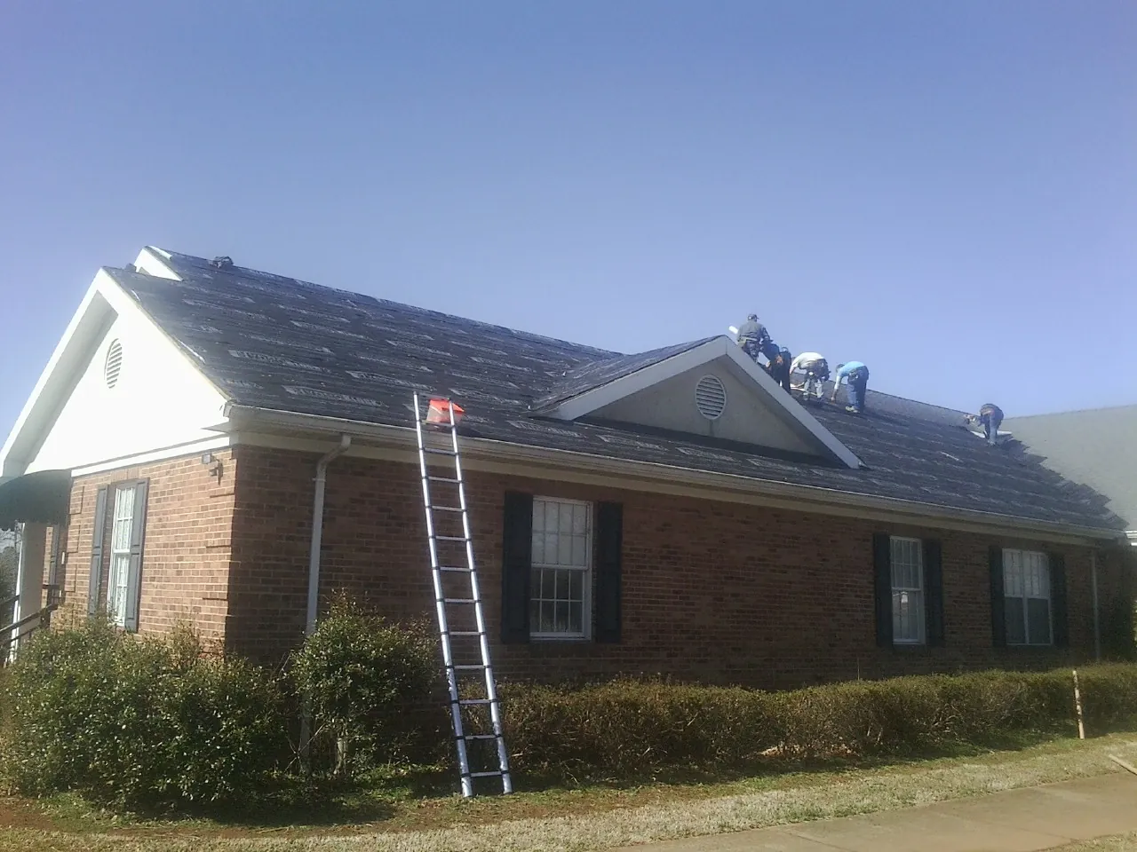 Crew tearing shingles off a brick ranch roof with a ladder set — Emergency Roof Repair work by our crew in Valley Springs