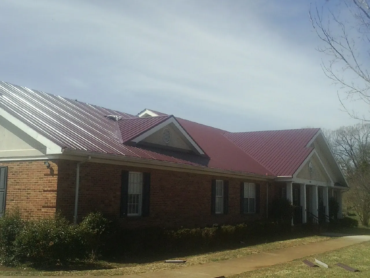 Red metal roof with gabled entries on a long brick building, from a Hail Damage Roof Repair job in Valley Springs
