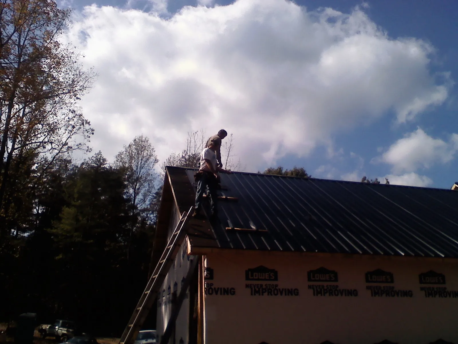 Roofer fastening dark metal panels high against a cloudy sky in Valley Springs