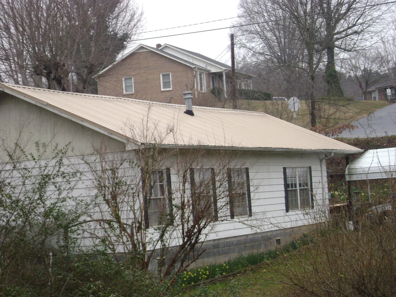 Tan metal roof on a white sided house set into a hillside — Commercial Roofing by Roofing Brothers in Valley Springs